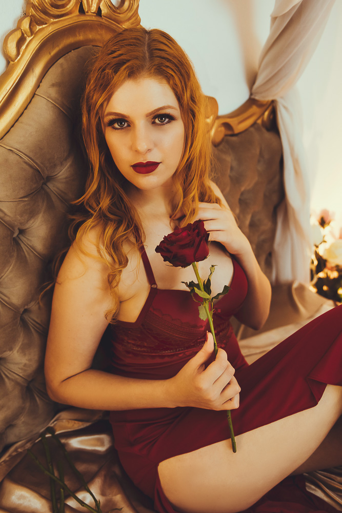 Mulher segurando uma rosa sentada na cama vestindo camisola vermelha
