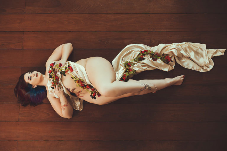 Fotografia aérea de mulher usando lençol no corpo com rosas vermelhas espalhadas em pose de ensaio boudoir sensual